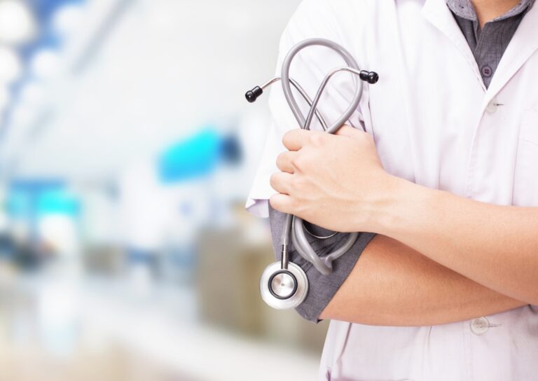 Lekarz w białym fartuchu trzyma stetoskop na tle rozmytego wnętrza szpitala.